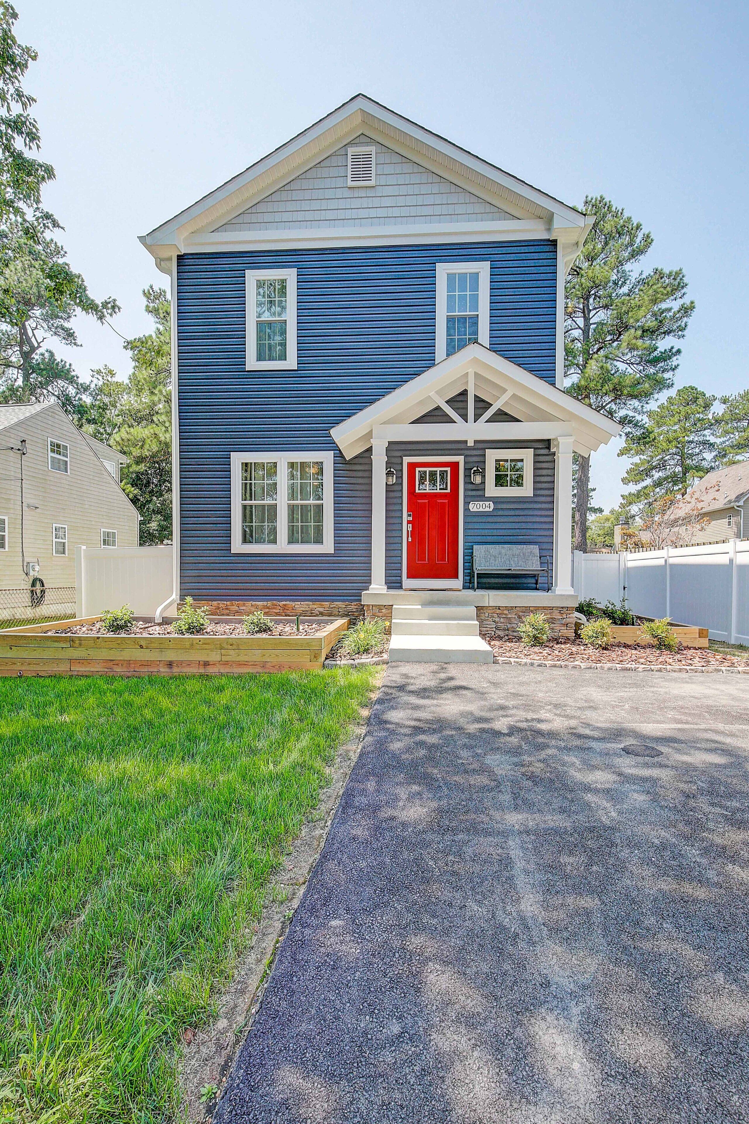 A two-story house with a red front door, a number '7004' on the door, and a small bench outside.