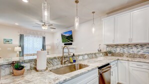 A modern kitchen with white cabinets, a marble countertop, a built-in dishwasher, and pendant lighting. - Harbor Breezes at Herrington Harbor (North Beach)