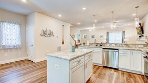 A modern kitchen with white cabinetry, a built-in dishwasher, and a marble countertop. - Harbor Breezes at Herrington Harbor (North Beach)