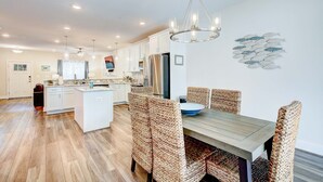 A modern kitchen with white cabinets, a central island, and a dining area with wicker chairs and a wooden table. - Harbor Breezes at Herrington Harbor (North Beach)