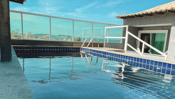 A swimming pool with clear blue water, tiled edges, and a glass barrier. - Pousada São Pedro (Sao Pedro da Aldeia)