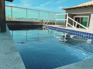 A swimming pool with clear blue water, tiled edges, and a glass barrier. - Pousada São Pedro (Sao Pedro da Aldeia)