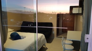 A hotel room with a bed, a small table, and a chair. There is a view of the sunset through the window. - Pousada São Pedro (Sao Pedro da Aldeia)