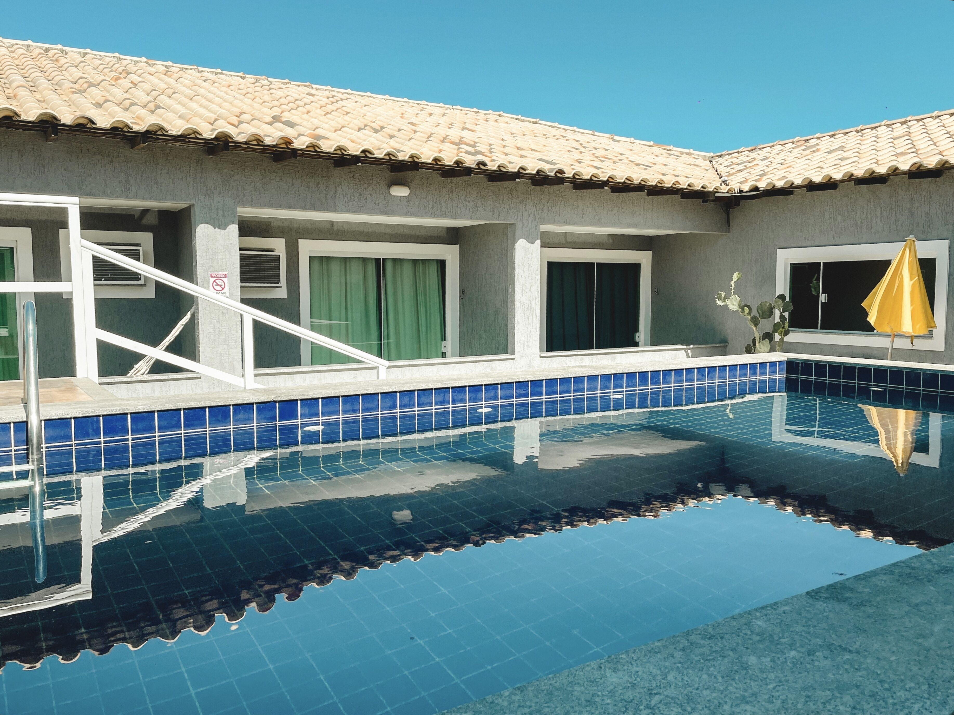A swimming pool with blue tiles, a tiled roof, and a yellow umbrella.