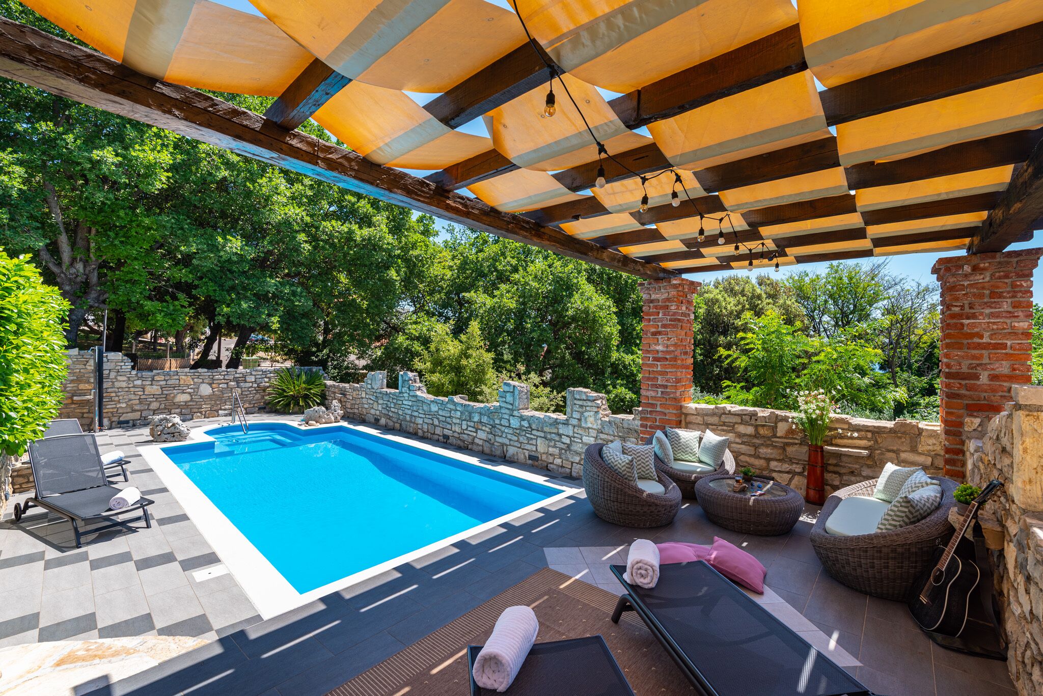 Un espace piscine doté d’une piscine à l’eau cristalline, de meubles en osier et d’une pergola illuminée de guirlandes lumineuses.