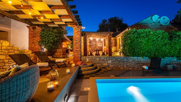 Un área de piscina con un muro de piedra, una silla de descanso y una mesa con velas.