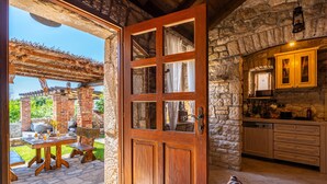 Una cocina rústica de piedra con armarios de madera y una puerta de madera que da a un patio exterior con una mesa y sillas.
