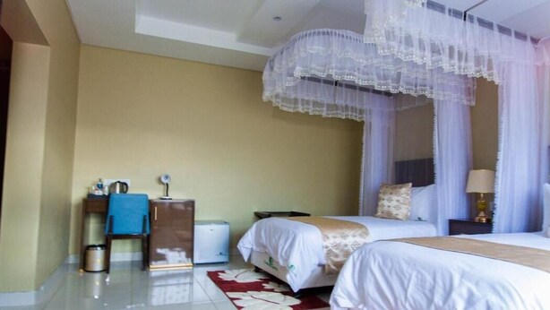 A hotel room with two beds, a bedside table with a lamp, a small table with a blue cloth, and a trash bin. - Chikho Hotel Mponela (Mponela)