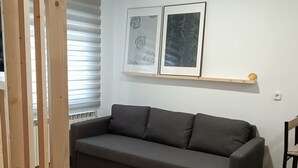 Uma sala de estar moderna com um sofá cinza escuro, piso de madeira e uma luminária no teto.