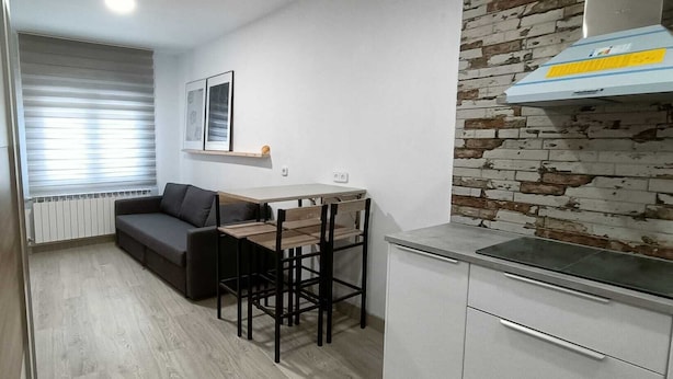 Cozinha compacta com mesa e cadeiras, um sofá e parede com padrão de tijolos.
