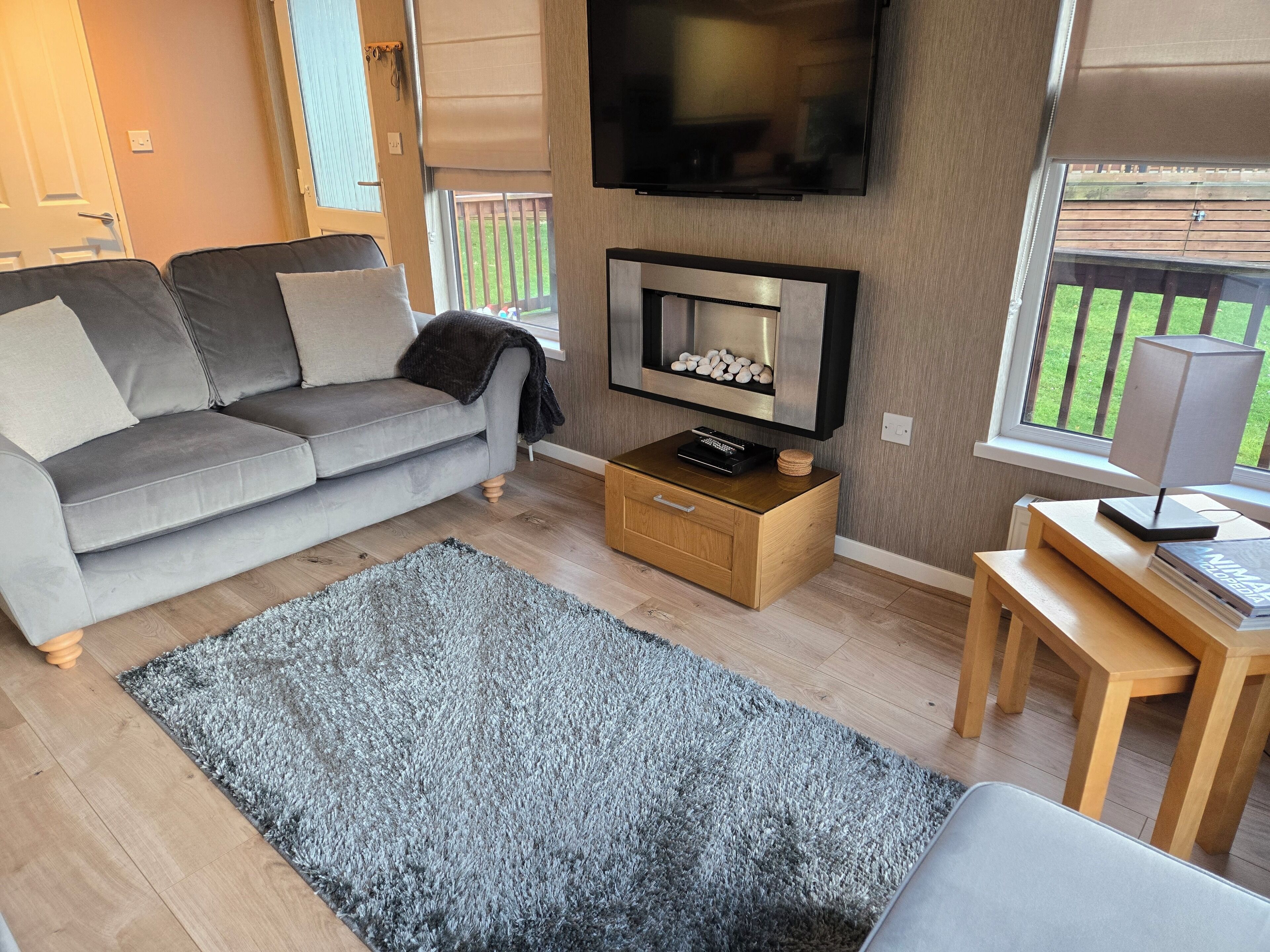 Una sala de estar moderna con un sofá gris, un televisor de pantalla plana, una mesa de centro de madera y una alfombra gris.
