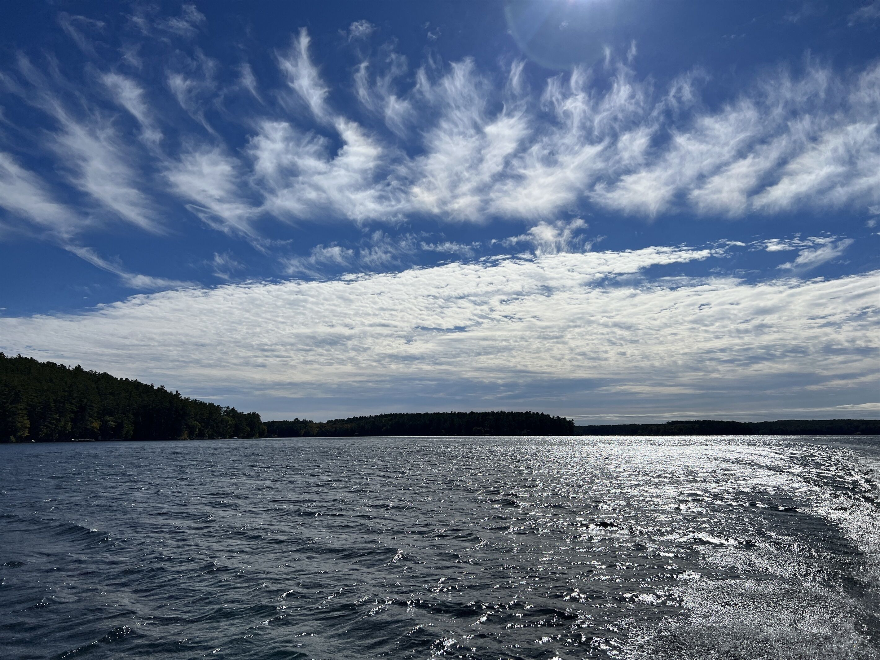 Une étendue d’eau calme, bordée d’une forêt, sous un ciel partiellement nuageux.