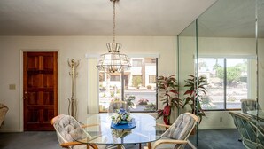 Zona pranzo con tavolo in vetro, sedie in vimini, lampadario e vista su un edificio e un paesaggio attraverso una porta in vetro.