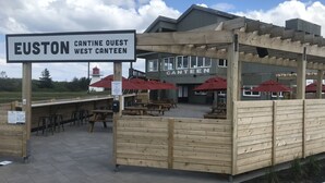 A wooden outdoor seating area with tables and red umbrellas at Euston West Canteen.