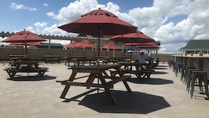 An outdoor patio with wooden picnic tables and red umbrellas.