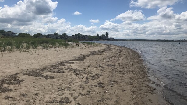 A beach with a sandy shore, a wooden bridge, and houses in the background.