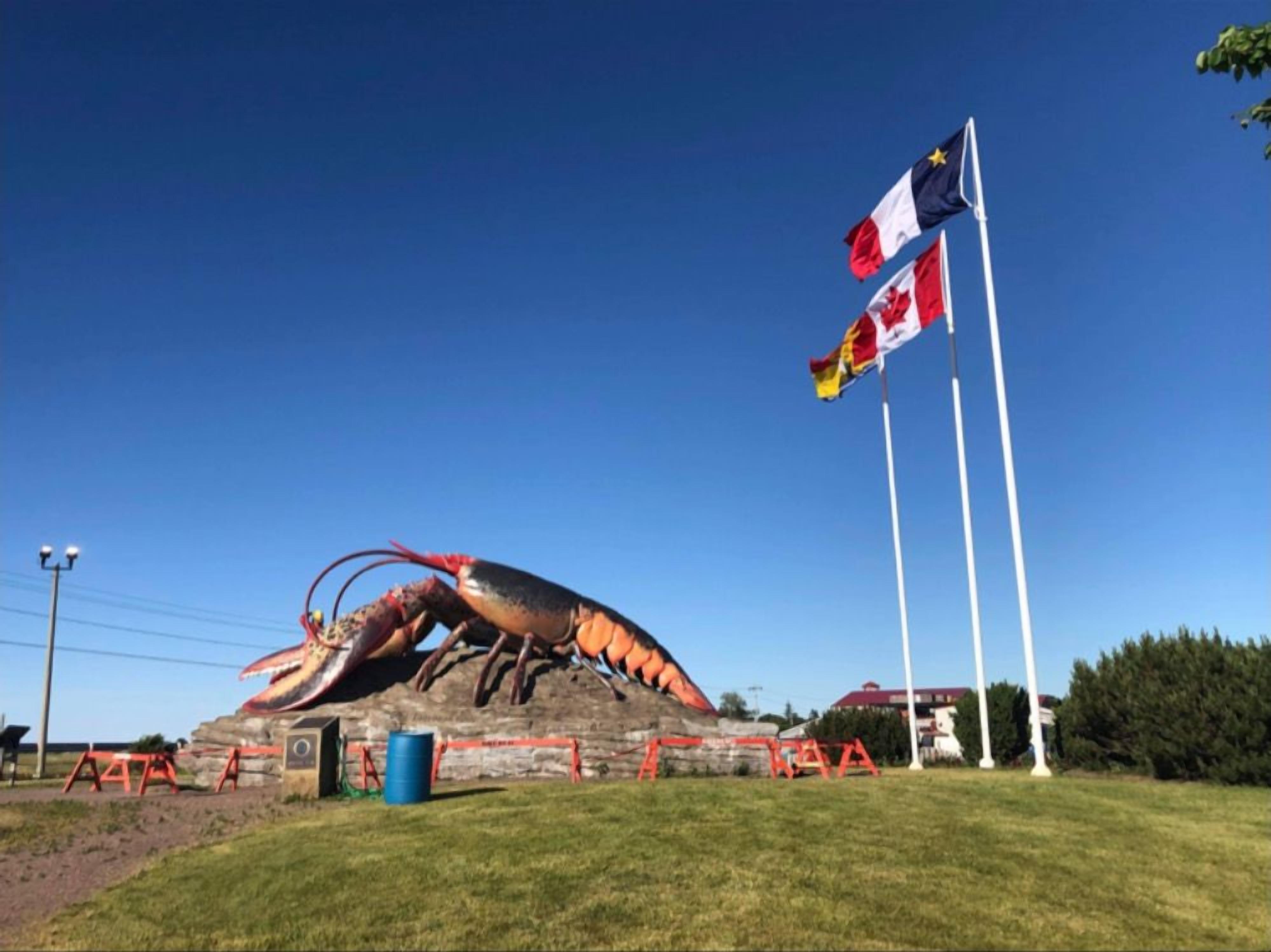 A large lobster sculpture on a grassy field with Canadian flags in the background.