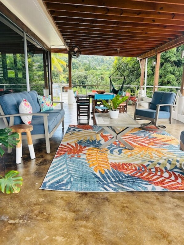 Relax in this serene outdoor seating area with a sofa, stool, and dining table amidst lush greenery.