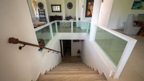 Eine Treppe mit Glastrennstäben führt zu einer Empfangshalle mit einer Couch und einem Gemälde.
