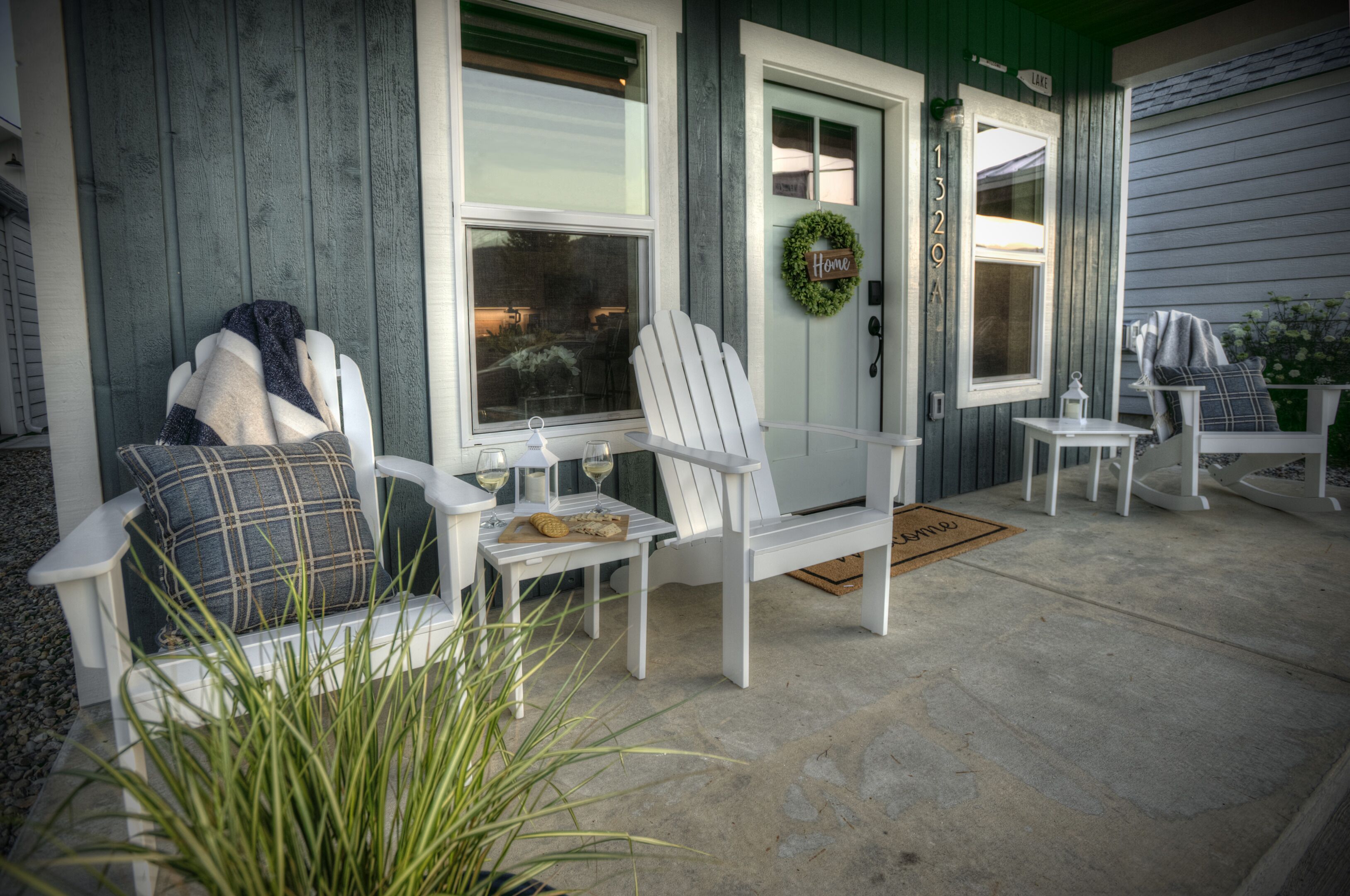 Une véranda avec deux fauteuils Adirondack blancs, une petite table avec un verre de vin et une guirlande sur la porte.