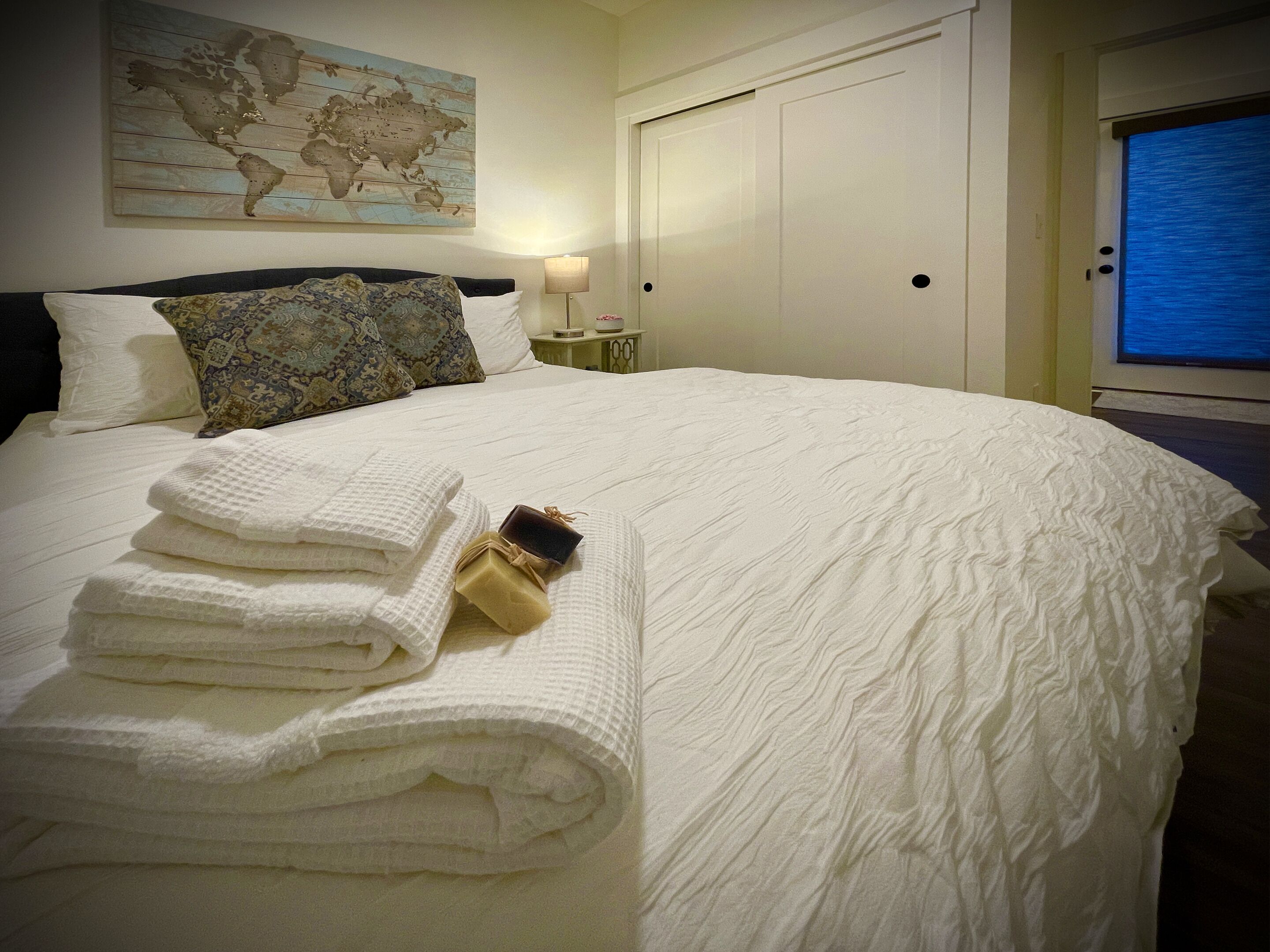 A neatly made bed with white linens, a world map on the wall, and a closed door.