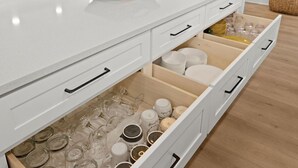 Una cucina moderna con mobili bianchi, un'isola ampia con un cesto in vimini e illuminazione a sospensione.