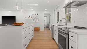 Una cucina moderna con mobili bianchi, una grande isola con cesto, luci a sospensione e forno integrato.