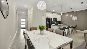 A modern kitchen with white cabinets, a central island with bar stools, and a dining area with a marble table and chairs.