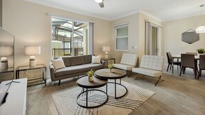 A modern living room with a sofa, two round coffee tables, a ceiling fan, and a dining area with chairs and a table.