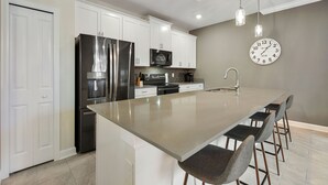 A modern kitchen with white cabinets, stainless steel appliances, a central island with bar stools, and pendant lighting.