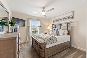 A bedroom with a bed, a ceiling fan, a dresser, a window with curtains, and a painting on the wall. - Private Pool with Premium Resort Ammenities Close By! (Kissimmee)