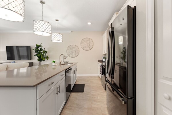 A modern kitchen with a large island, stainless steel appliances, pendant lighting, and decorative wall art. - Private Pool with Premium Resort Ammenities Close By! (Kissimmee)