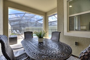 A covered outdoor patio with a round metal table, two chairs, and a potted plant. - Private Pool with Premium Resort Ammenities Close By! (Kissimmee)