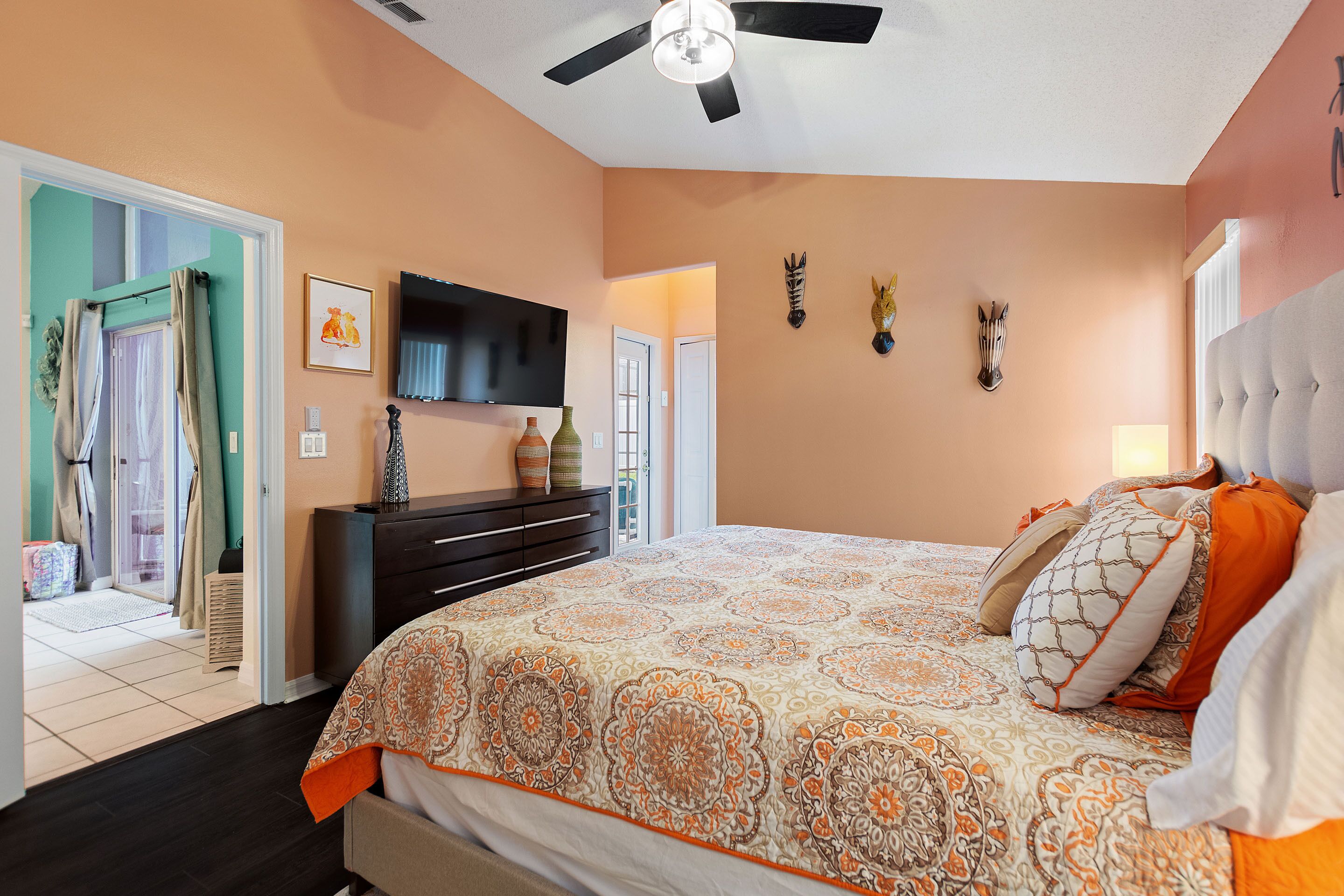 A bedroom with a large bed, a ceiling fan, a flat-screen TV, and a dresser.