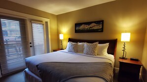 Een hotelkamer met een groot bed, twee bedlampen, een schilderij aan de muur en een deur met zonwering.