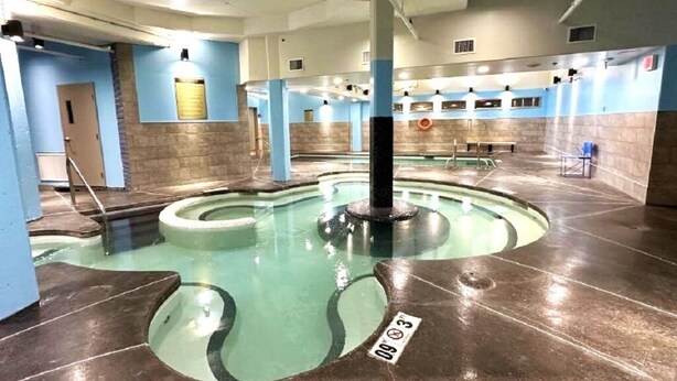 Een binnenzwembad met een centrale kolom, betegelde wanden en een helder watergedeelte.