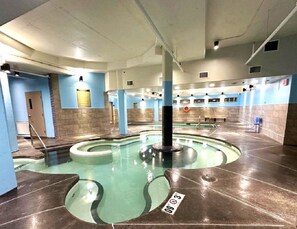 An indoor swimming pool with a central column, tiled walls, and a clear water area.