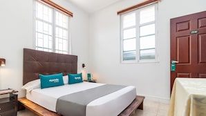 A hotel room with a large bed, two windows, a wooden headboard, a bedside table, and a nightstand. - Ayenda Eloina (Bogotá)