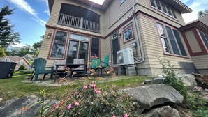 Een tweelaags huis met een balkon, grote ramen en een kleine tuin met bloemen en rotsen.