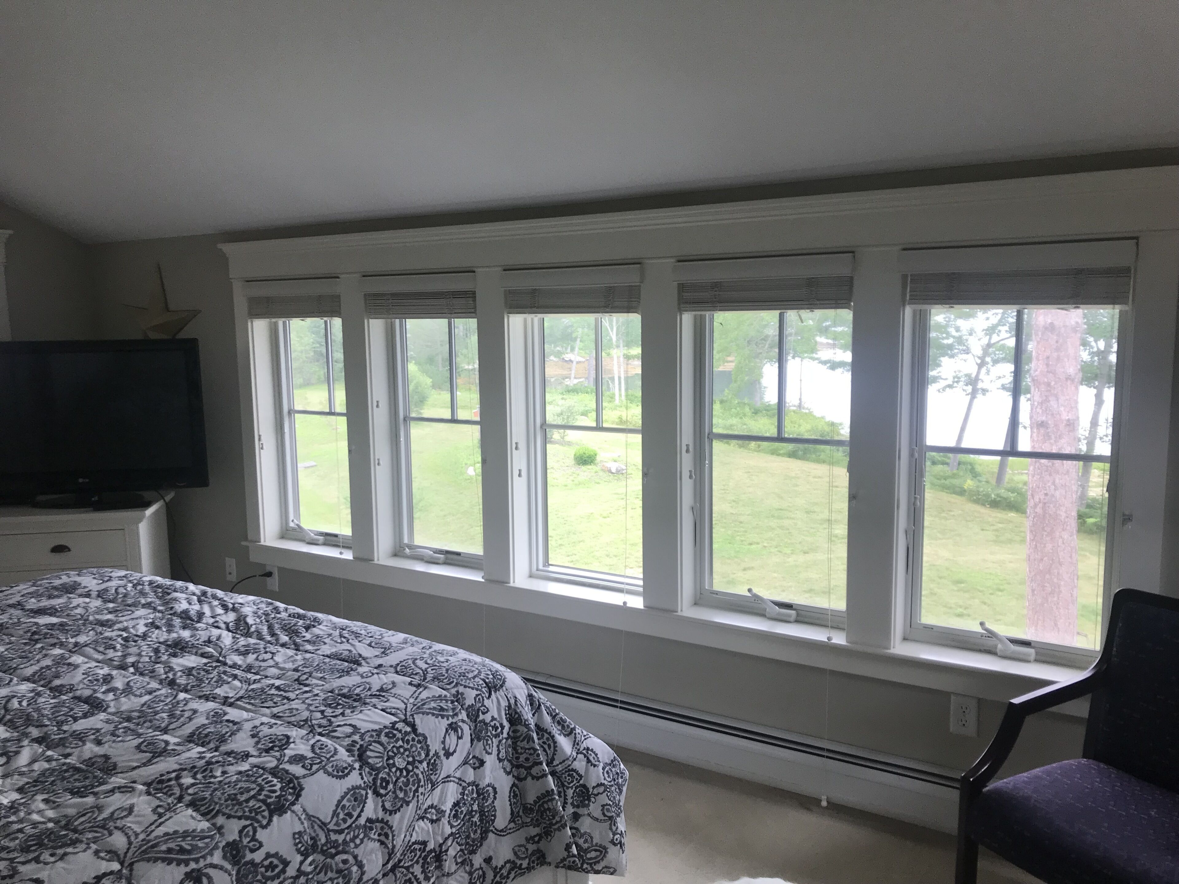 A bedroom with a large bed, a TV on a dresser, and a window with a view of a yard.