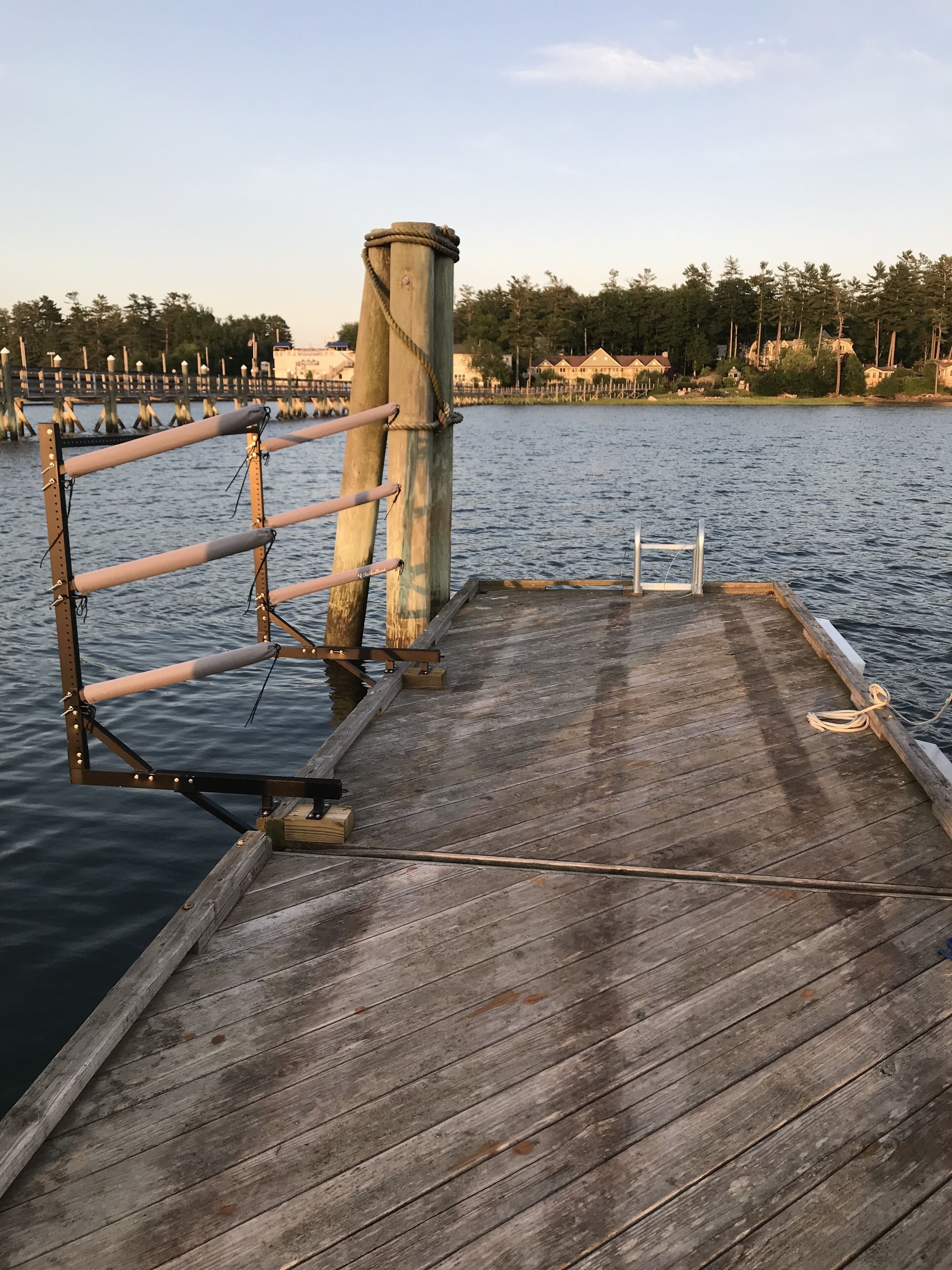 Un muelle de madera que se adentra en aguas tranquilas, con barandilla de metal y un poste de hormigón.