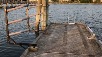 Un muelle de madera que se adentra en aguas tranquilas, con barandilla de metal y un poste de hormigón.
