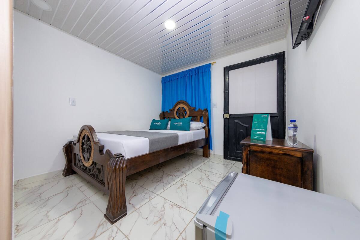 A bedroom with a wooden bed, a desk, a chair, a wardrobe, and a bathroom door.