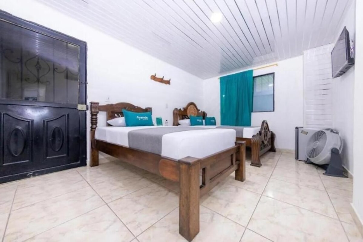 A bedroom with a wooden bed, a black wardrobe, a fan, and a window with curtains.