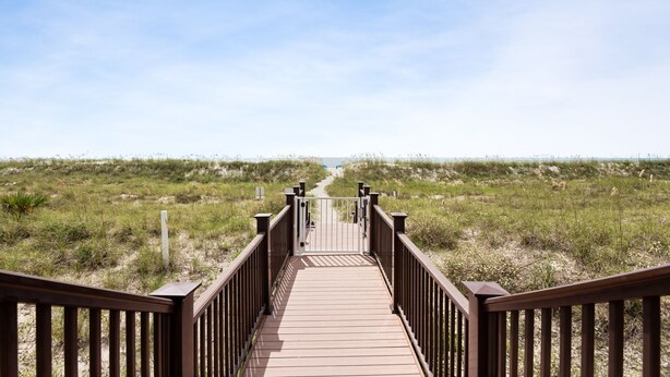 Een houten looppad dat naar een strand met duinen en gras leidt.