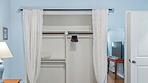 A bedroom with a wardrobe, a bedside table with a lamp, and a television in the corner.
