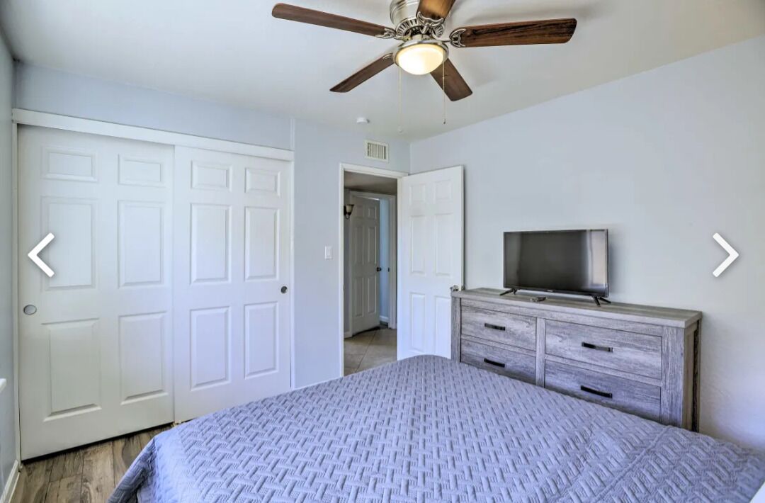 A bedroom with a bed, a dresser, a ceiling fan, and a television.