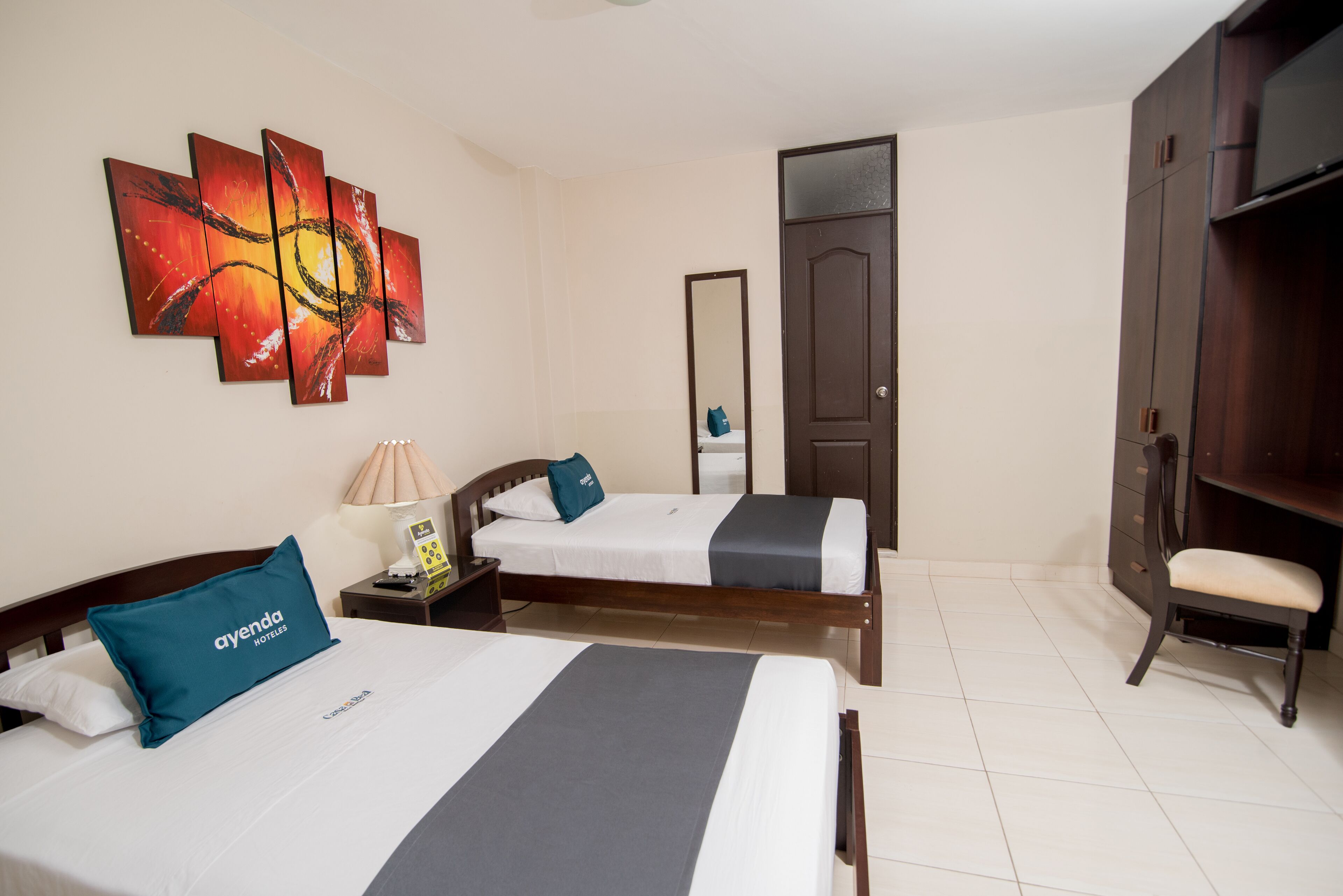 A hotel room with two beds, a large mirror, a wardrobe, and a painting on the wall.
