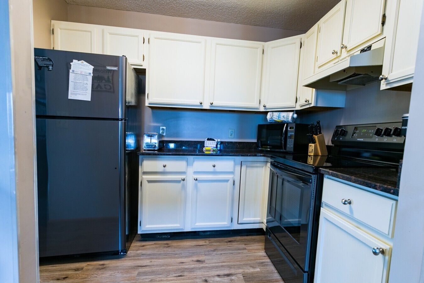 A compact kitchen with white cabinets, a black refrigerator, a microwave, and a stove.