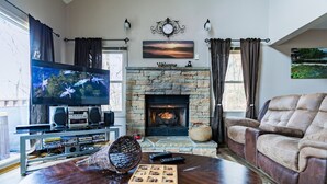 A living room with a stone fireplace, a television, a fireplace screen, and a comfortable seating area. - Sauna + Hot Tub | Mtn Views | Pet-Friendly Cabin (Gatlinburg)